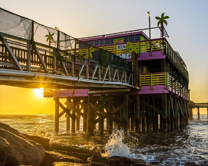 The pink and yellow pier building at sunrise, waves breaking on the rocks